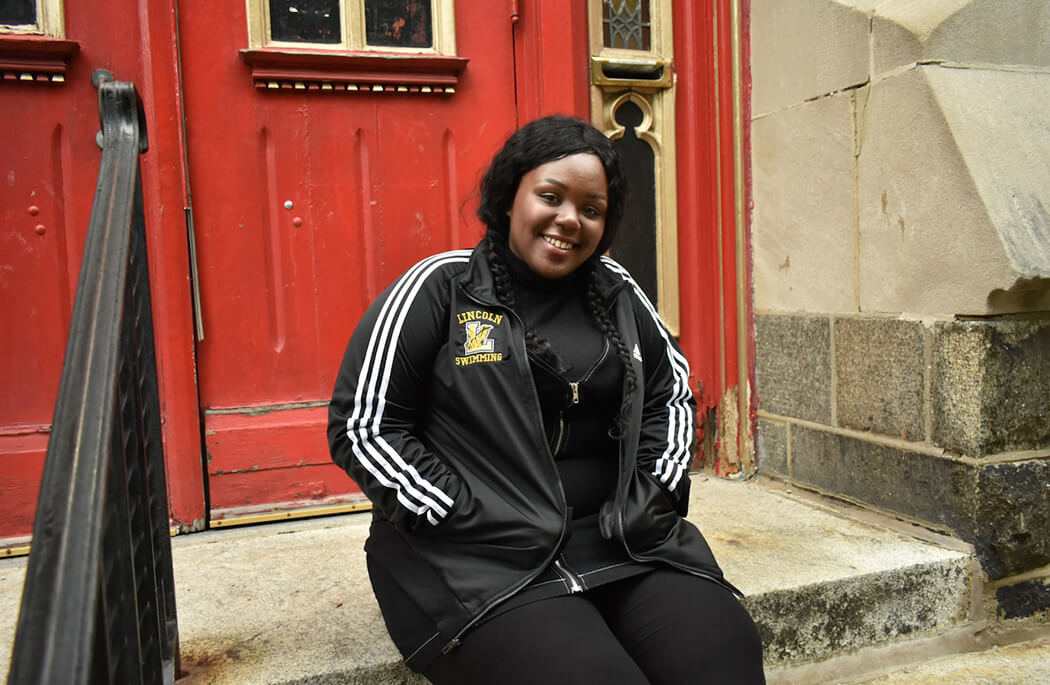 A young person sitting on the steps of a doorway.